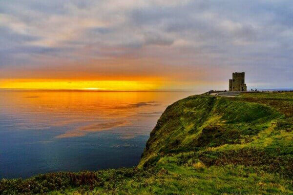 sunset over the ocean with a cliff tower nearby the Cliffs of Moher