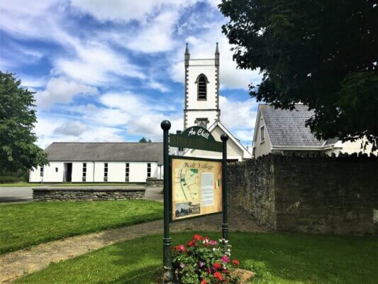 a sign with flowers in front of it and a church in the background Saint Brigid