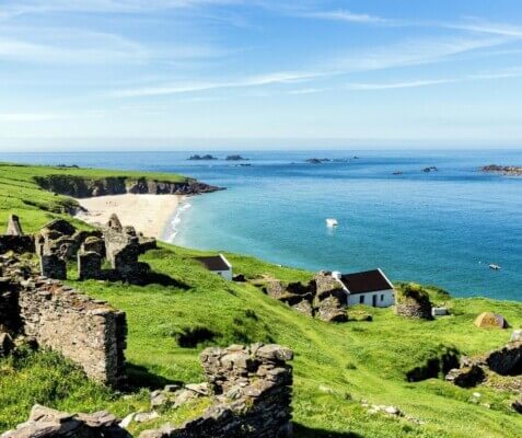 an old building with the beach and ocean in the background Experience the Great Blasket Island