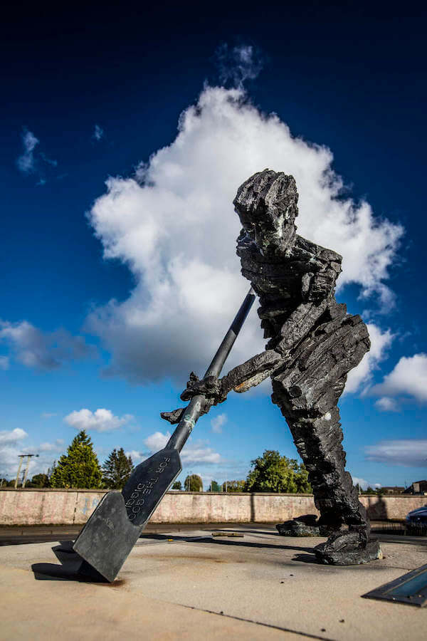 a statue of a man with a shovel 3 Irish poets