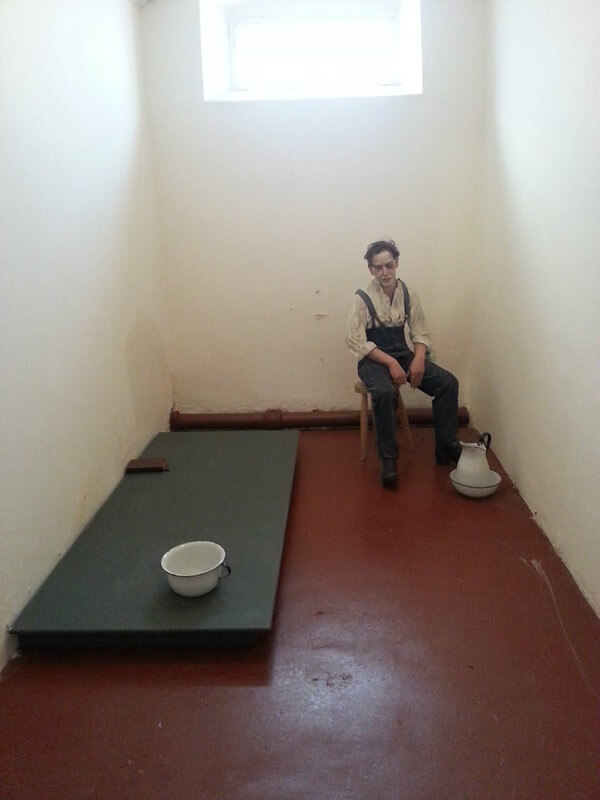 a wax figure sitting in a jail cell with a dish on the floor Belfast's Crumlin Road Gaol
