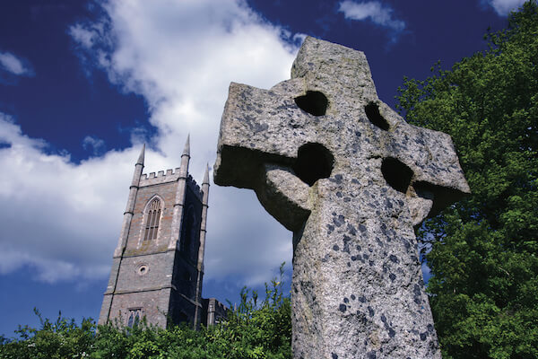 Celtic cross with a tower in the background Saint Patrick Centre